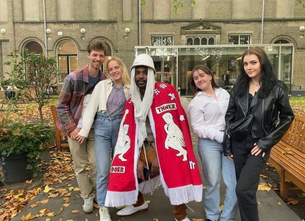 Take pARTners met kunstenaar Umar Rashid voor het Dordrechts Museum. Rashid draagt een rode omslagdoek en een witte tropenhelm.